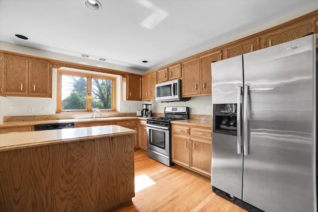 kitchen with brown cabinets, a sink, stainless steel appliances, light wood-style floors, and light countertops