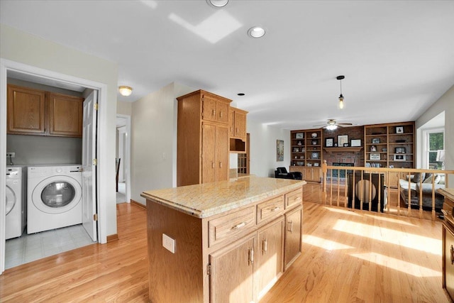 kitchen featuring light wood-type flooring, a center island, a fireplace, ceiling fan, and washing machine and clothes dryer