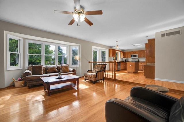 living area with visible vents, baseboards, light wood-style floors, and a ceiling fan