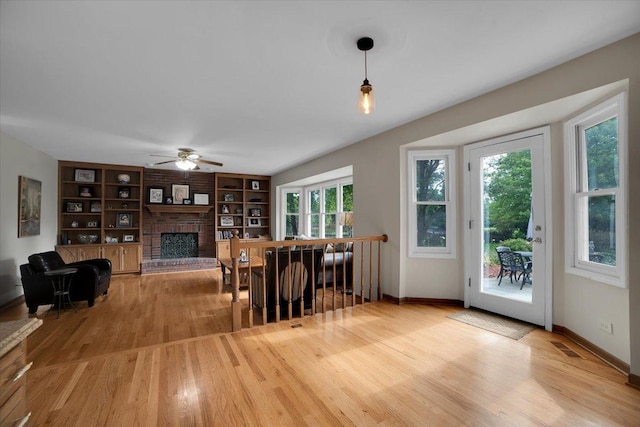 dining area with built in features, a ceiling fan, baseboards, light wood-style floors, and a brick fireplace