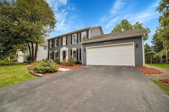 colonial-style house featuring aphalt driveway, a garage, and a front lawn