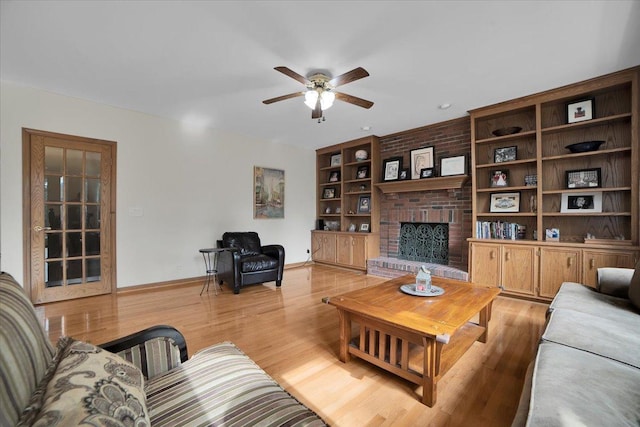 living area featuring built in features, baseboards, light wood-style flooring, a fireplace, and ceiling fan