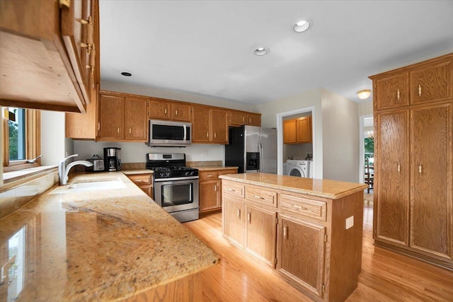 kitchen with a kitchen island, a sink, stainless steel appliances, washer and dryer, and light wood-type flooring