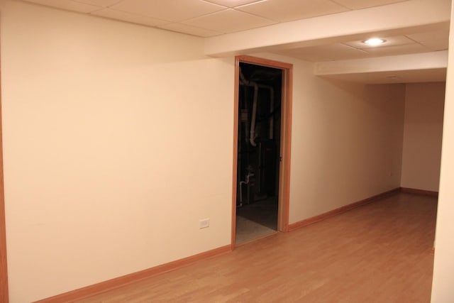 empty room featuring a drop ceiling, baseboards, and light wood finished floors