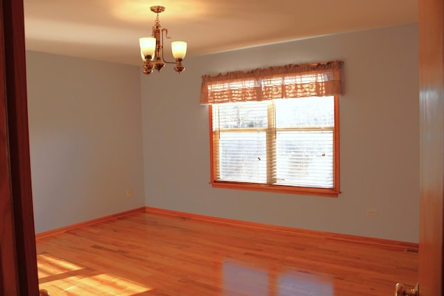 unfurnished room with an inviting chandelier, baseboards, and light wood finished floors