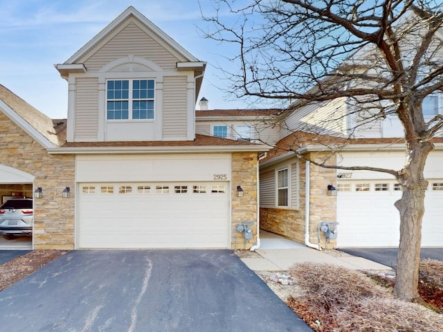 traditional home featuring aphalt driveway, an attached garage, and stone siding