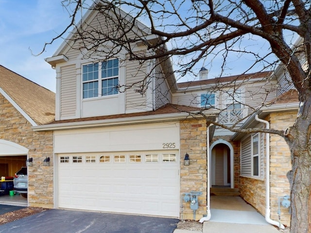 traditional-style house featuring aphalt driveway, roof with shingles, a chimney, stone siding, and an attached garage