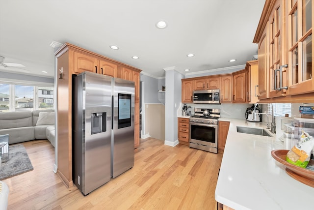 kitchen featuring ornamental molding, a sink, glass insert cabinets, appliances with stainless steel finishes, and light wood-type flooring