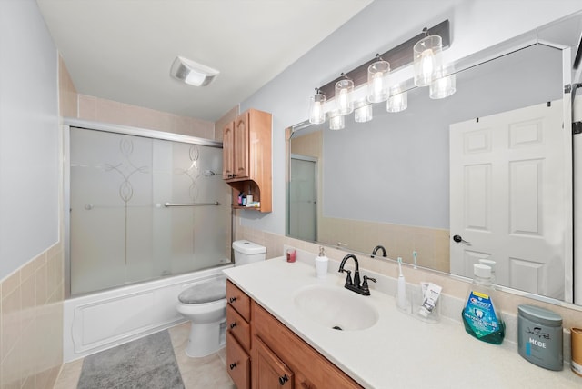 bathroom featuring toilet, vanity, shower / bath combination with glass door, tile patterned floors, and tile walls