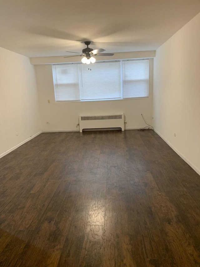 empty room with radiator, baseboards, ceiling fan, and dark wood-style flooring