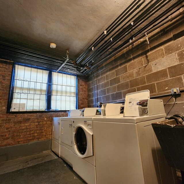 laundry area featuring a sink, brick wall, concrete block wall, and washer and clothes dryer