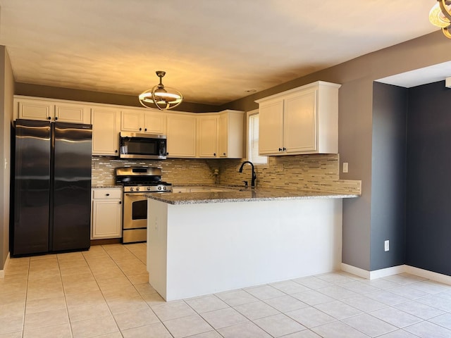 kitchen with a sink, dark stone countertops, tasteful backsplash, appliances with stainless steel finishes, and a peninsula