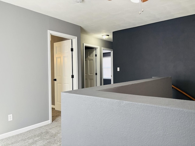 corridor featuring baseboards, an upstairs landing, and carpet flooring