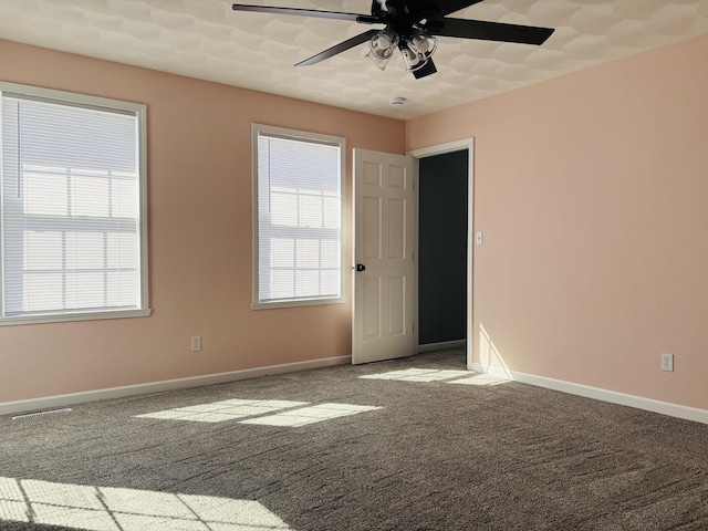 carpeted empty room featuring visible vents, a healthy amount of sunlight, a ceiling fan, and baseboards