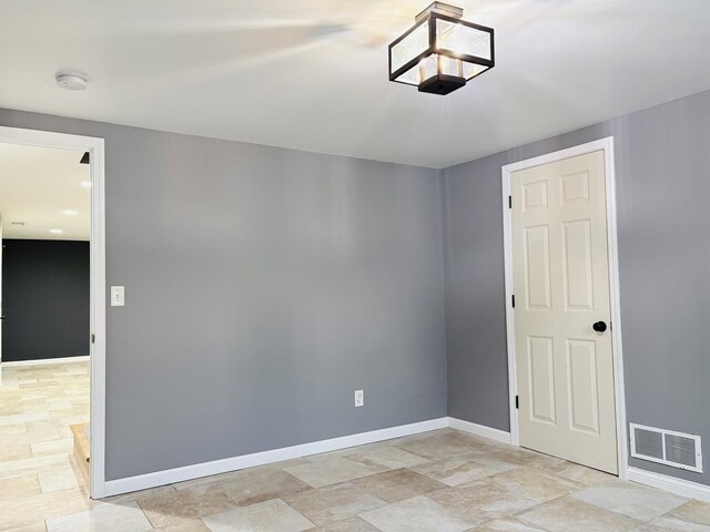 spare room featuring stone finish floor, baseboards, and visible vents