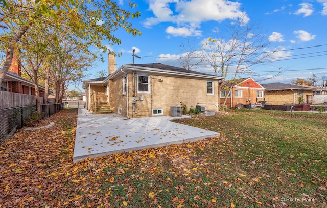 rear view of property with a yard, a fenced backyard, a chimney, central air condition unit, and brick siding