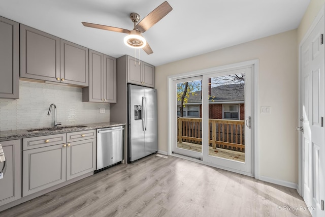 kitchen with light stone counters, decorative backsplash, gray cabinets, stainless steel appliances, and a sink