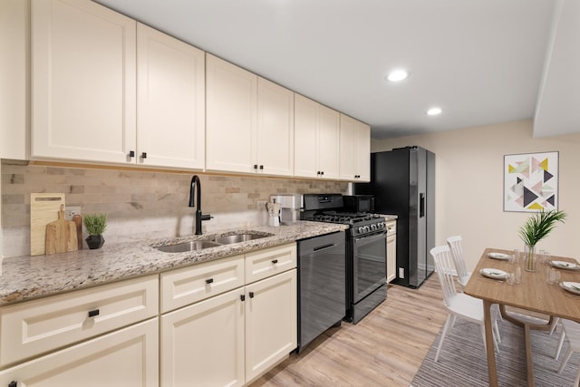 kitchen with light stone counters, light wood-style flooring, a sink, black appliances, and tasteful backsplash
