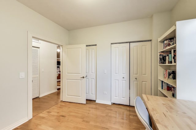 unfurnished bedroom with light wood-style flooring, two closets, and baseboards