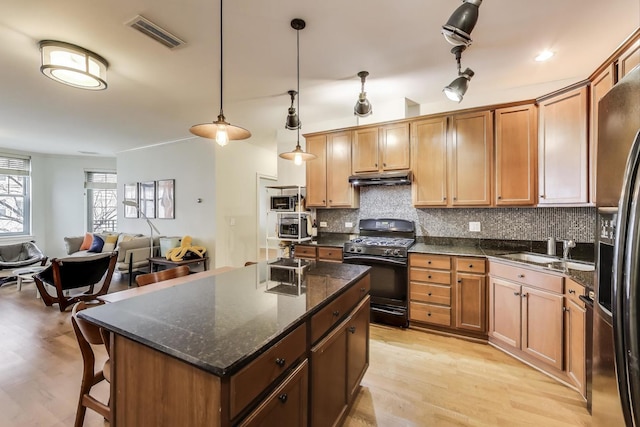 kitchen featuring visible vents, under cabinet range hood, decorative backsplash, gas stove, and a sink