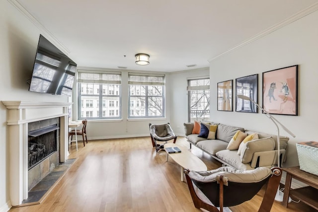 living area featuring baseboards, light wood finished floors, crown molding, and a tile fireplace