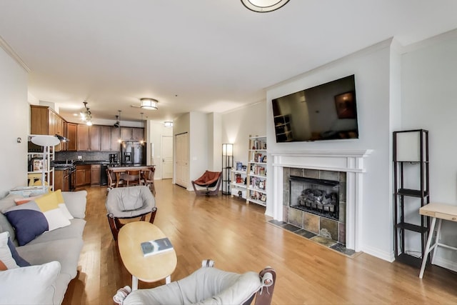 living area with a tile fireplace, baseboards, crown molding, and light wood-style floors