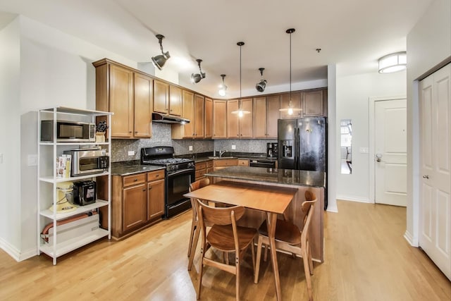 kitchen with under cabinet range hood, backsplash, light wood finished floors, and black appliances