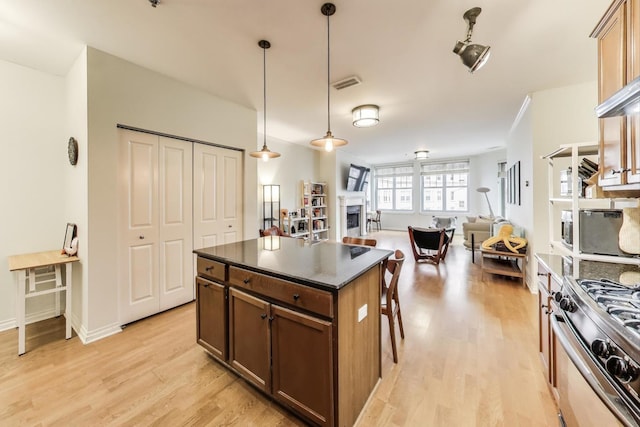 kitchen with dark countertops, visible vents, a fireplace, light wood-style floors, and gas range