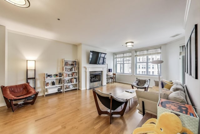 living area featuring light wood finished floors, visible vents, baseboards, ornamental molding, and a fireplace