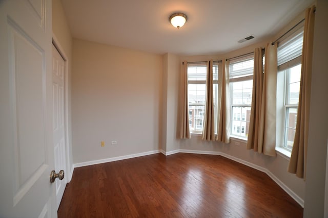 unfurnished room featuring dark wood finished floors, visible vents, and baseboards