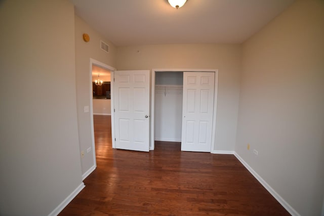 unfurnished bedroom with dark wood-style floors, visible vents, baseboards, a closet, and a notable chandelier