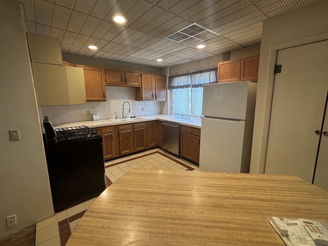 kitchen featuring a sink, stainless steel dishwasher, freestanding refrigerator, light countertops, and black range with gas cooktop