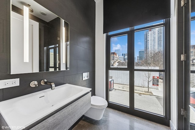 bathroom with concrete floors, a city view, toilet, tile walls, and a sink