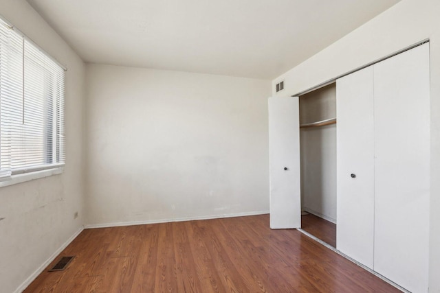 unfurnished bedroom featuring visible vents, baseboards, a closet, and wood finished floors