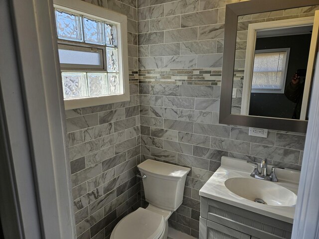 bathroom with toilet, tile walls, and vanity