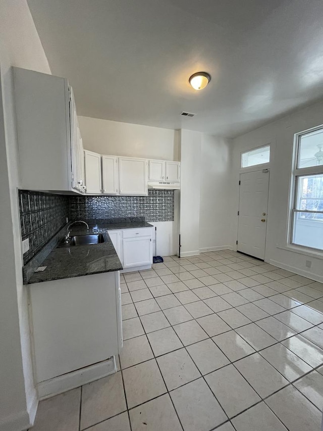 kitchen featuring light tile patterned floors, a sink, white cabinetry, dark countertops, and tasteful backsplash