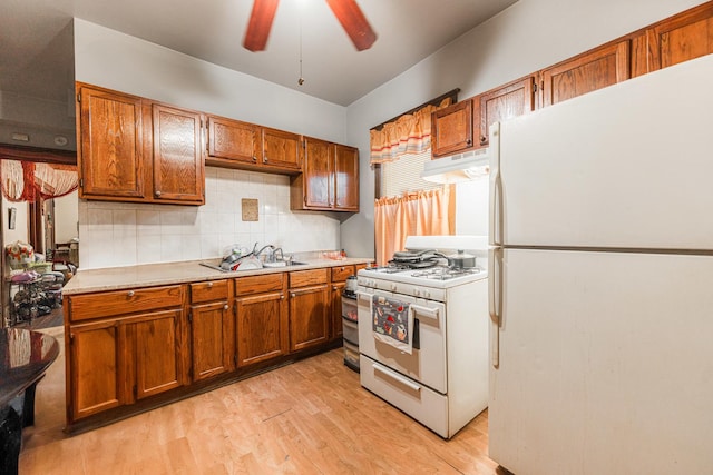 kitchen featuring a sink, white appliances, under cabinet range hood, and brown cabinetry