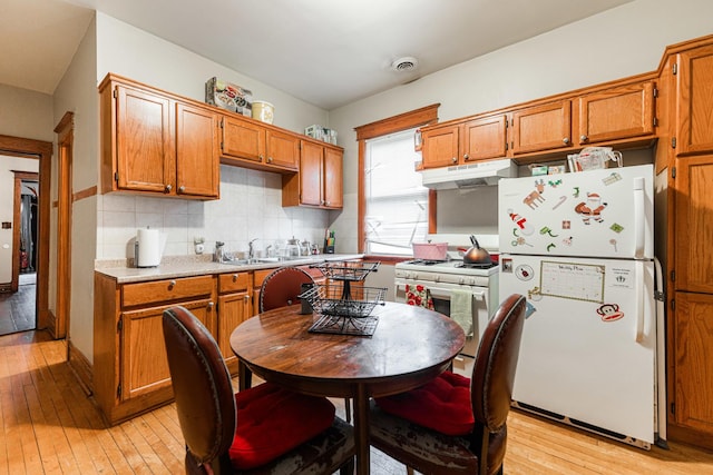 kitchen featuring light wood finished floors, under cabinet range hood, light countertops, decorative backsplash, and white appliances