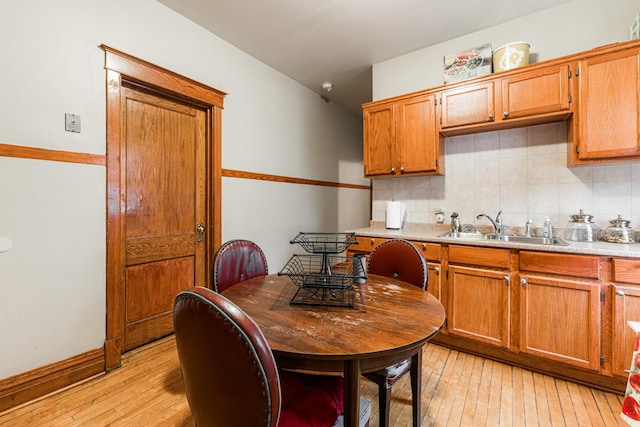 kitchen with light wood-type flooring, a sink, tasteful backsplash, brown cabinetry, and light countertops