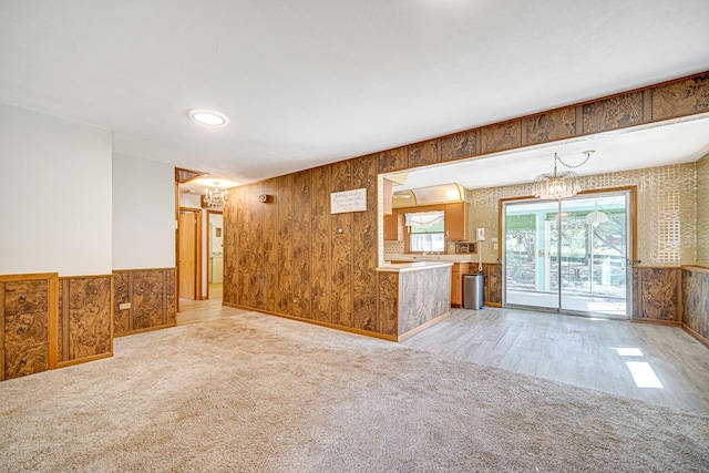 unfurnished living room featuring light carpet, a notable chandelier, and a wainscoted wall