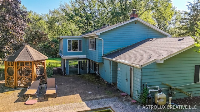 rear view of house with a shingled roof and fence