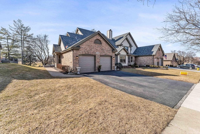 view of front of property featuring brick siding, a front lawn, a chimney, a garage, and driveway