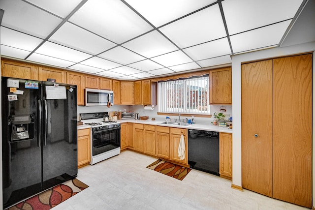 kitchen with black appliances, a paneled ceiling, light countertops, and a sink