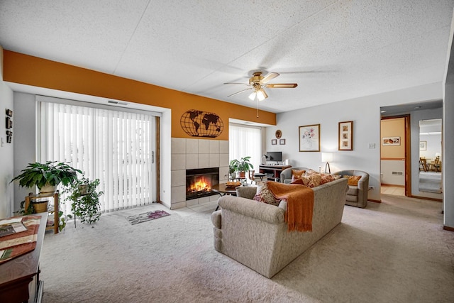 carpeted living room with a tiled fireplace, a healthy amount of sunlight, a textured ceiling, and ceiling fan