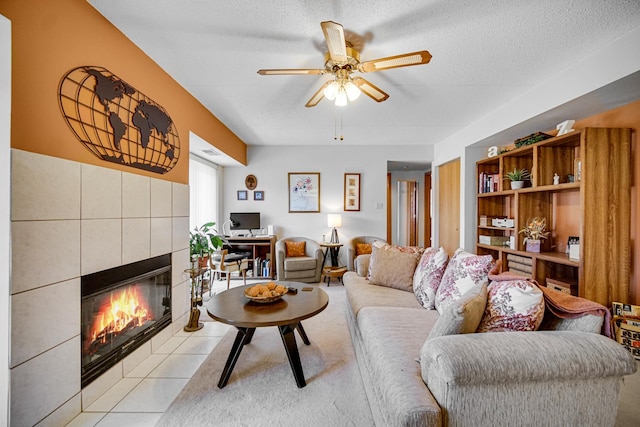 living area featuring a tiled fireplace, ceiling fan, light tile patterned floors, and a textured ceiling