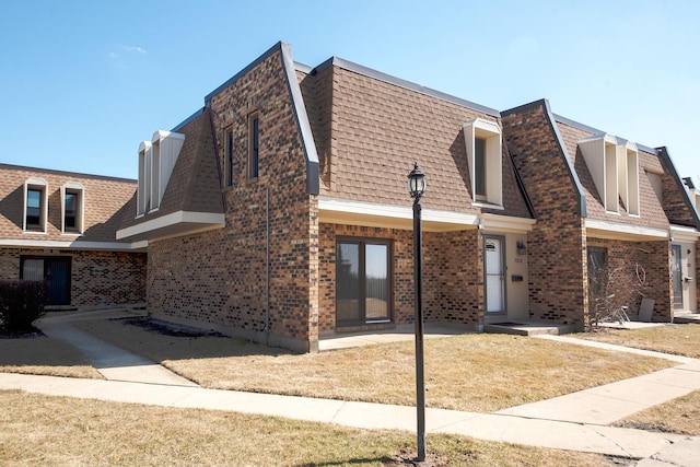 view of property featuring a front yard, brick siding, and a shingled roof