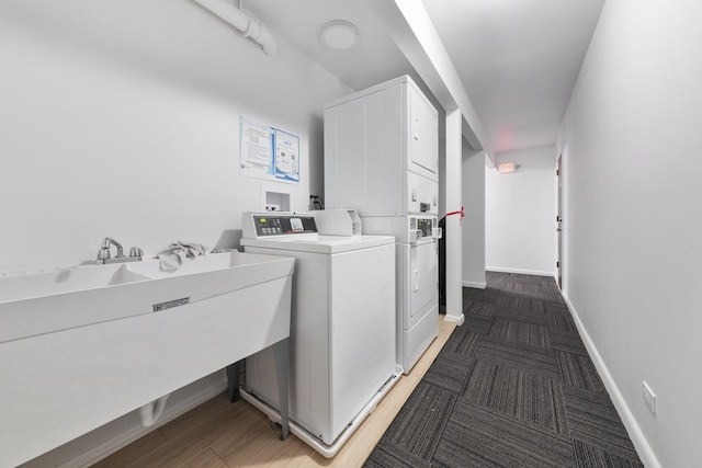 shared laundry area with baseboards, stacked washing maching and dryer, a sink, light carpet, and washer and clothes dryer