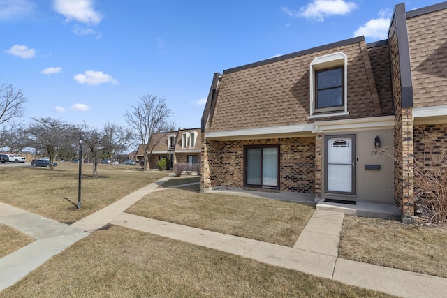 view of front of property with mansard roof, brick siding, and a shingled roof