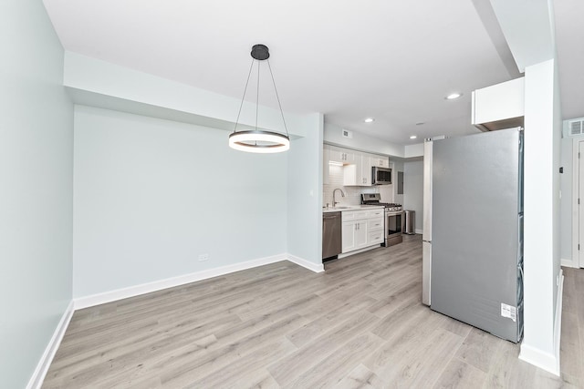 kitchen with light wood finished floors, a sink, light countertops, appliances with stainless steel finishes, and backsplash