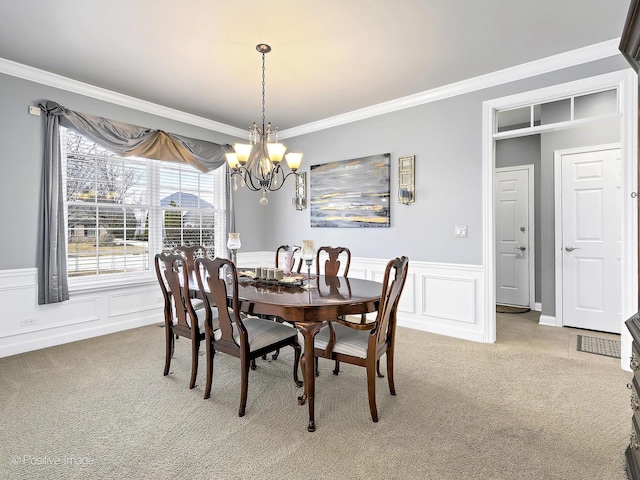 carpeted dining area with a decorative wall, a wainscoted wall, a chandelier, and ornamental molding